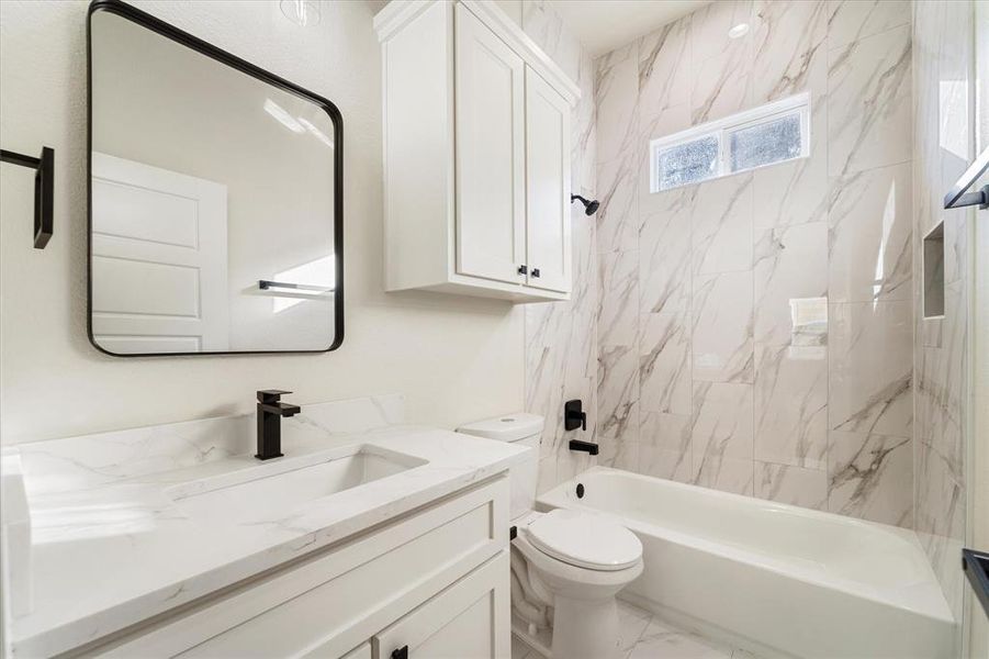 The full bathroom features crisp white & grey tile flooring, a sleek vanity, and a luxurious quartz countertop. The shower-tub combo is fully tiled, offering the perfect balance of convenience for quick showers and relaxation for baths.