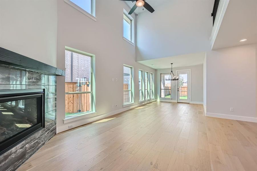 Unfurnished living room with ceiling fan with notable chandelier, light wood-type flooring, and a high ceiling