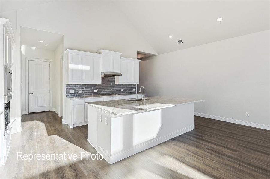 Kitchen featuring light stone countertops, high vaulted ceiling, a kitchen island with sink, and wood-type flooring