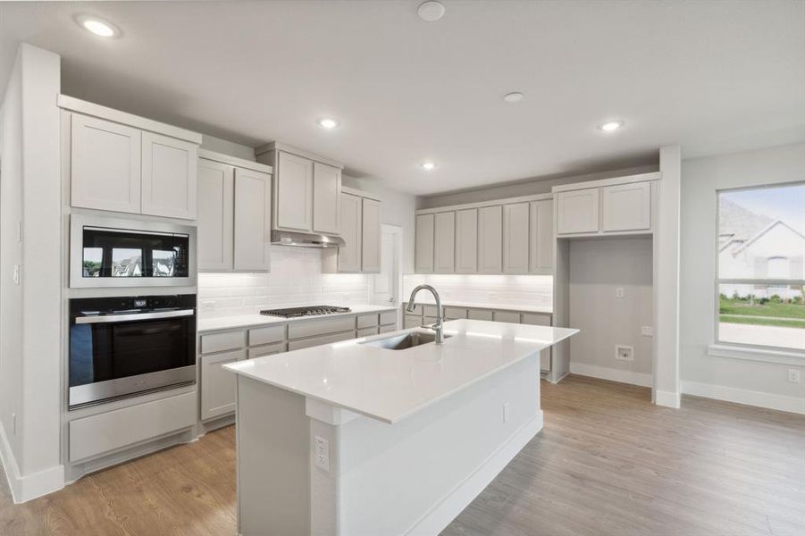 Kitchen featuring stainless steel appliances, light hardwood / wood-style floors, sink, an island with sink, and decorative backsplash