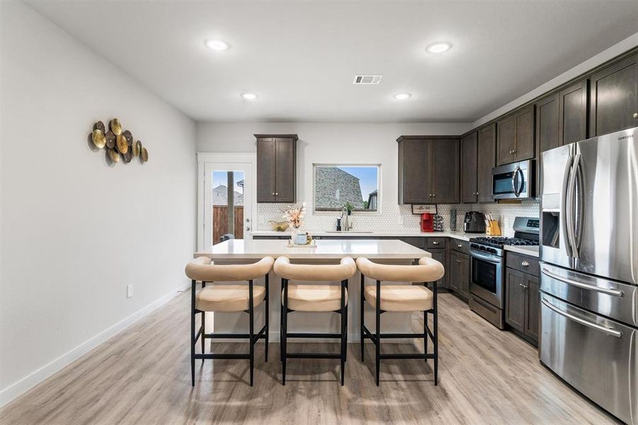 Kitchen with dark brown cabinets, appliances with stainless steel finishes, light wood-type flooring, and a kitchen island