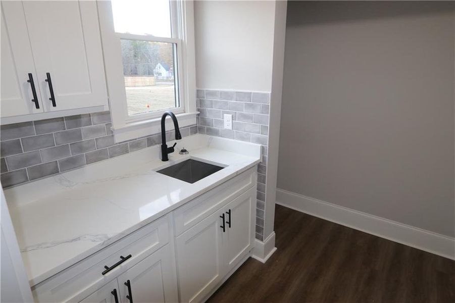 Kitchen with sink, tasteful backsplash, light stone counters, white cabinets, and dark hardwood / wood-style floors