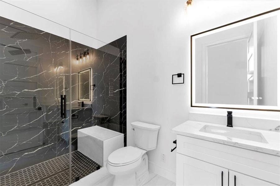 The first bedroom's en-suite bathroom has an anti-fog LED mirror, quartz countertop, matte black hardware and large walk-in, frameless glass shower with rain shower head and shampoo inset.