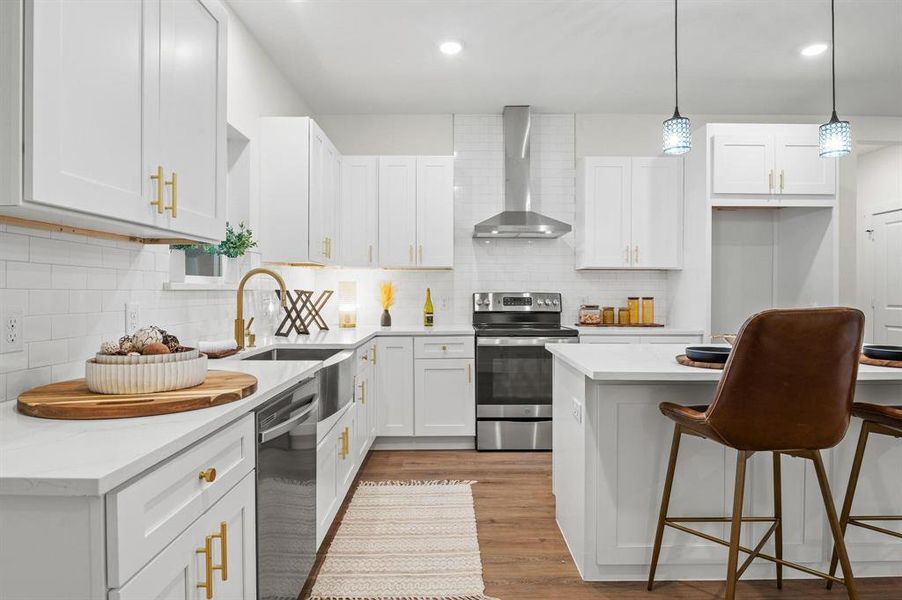 Kitchen featuring light wood-type flooring, white cabinetry, stainless steel appliances, wall chimney exhaust hood, and decorative light fixtures