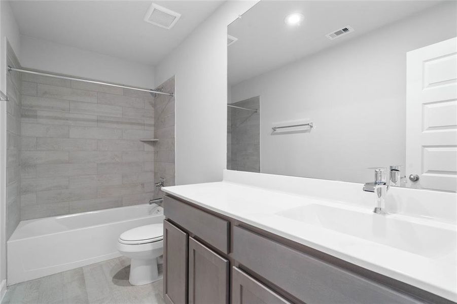 Secondary bath features tile flooring, bath/shower combo with tile surround, stained wood cabinets, beautiful light countertops, mirror, sleek fixtures and modern finishes.