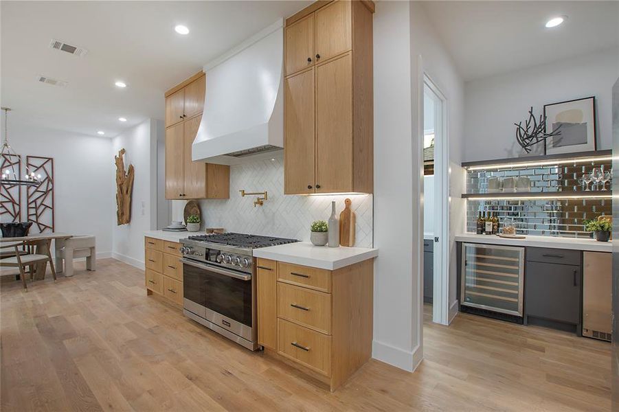 Kitchen featuring custom range hood, high end stove, light wood-type flooring, and beverage cooler