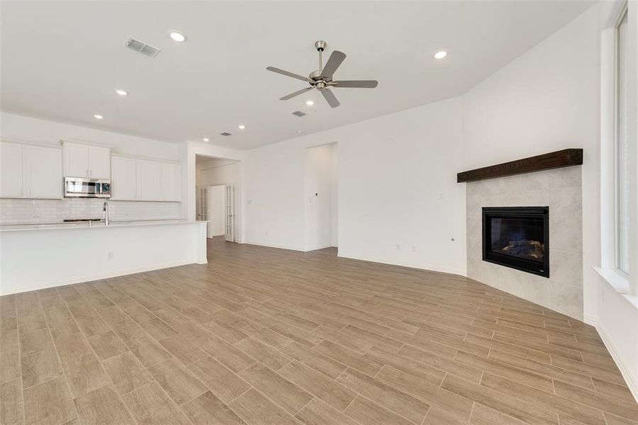 Unfurnished living room with light hardwood / wood-style floors, a tiled fireplace, and ceiling fan