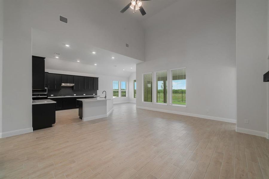 Kitchen with light hardwood / wood-style flooring, ceiling fan, high vaulted ceiling, and a kitchen island with sink