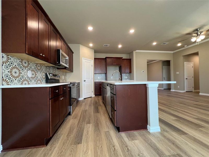 Kitchen featuring light wood-type flooring, a kitchen island with sink, tasteful backsplash, appliances with stainless steel finishes, and ceiling fan