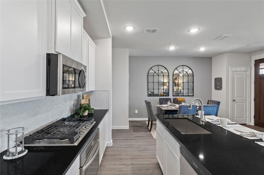 Kitchen featuring light wood-type flooring, tasteful backsplash, sink, appliances with stainless steel finishes, and white cabinets