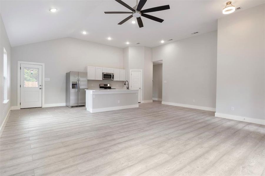 Unfurnished living room featuring high vaulted ceiling, ceiling fan, sink, and light hardwood / wood-style flooring