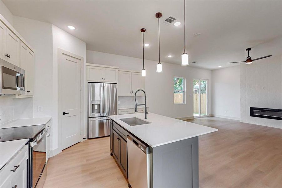 Kitchen with sink, pendant lighting, white cabinetry, appliances with stainless steel finishes, and a center island with sink