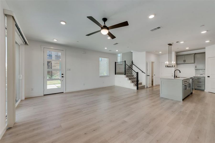 Unfurnished living room featuring sink, ceiling fan with notable chandelier, and light wood-type flooring