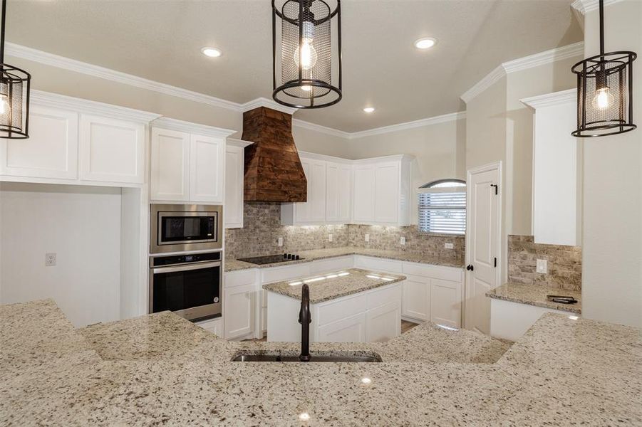 Kitchen featuring stainless steel appliances, white cabinetry, and hanging light fixtures