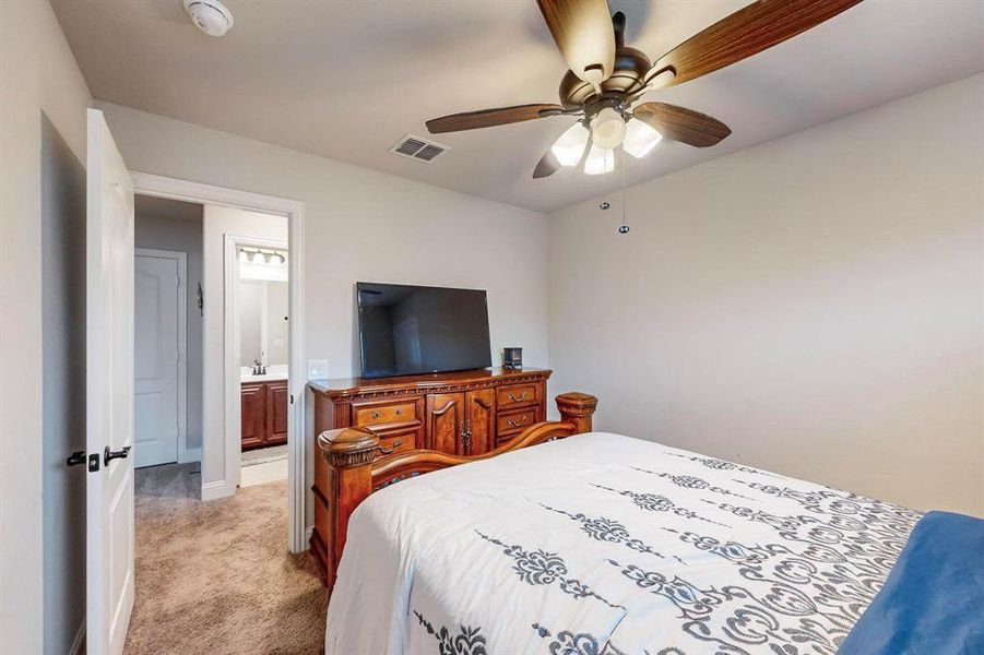 Bedroom with ensuite bathroom, ceiling fan, and light carpet