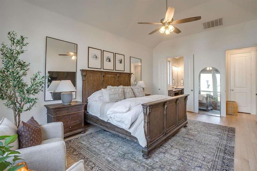 Bedroom featuring ceiling fan, vaulted ceiling, ensuite bathroom, and light hardwood / wood-style flooring