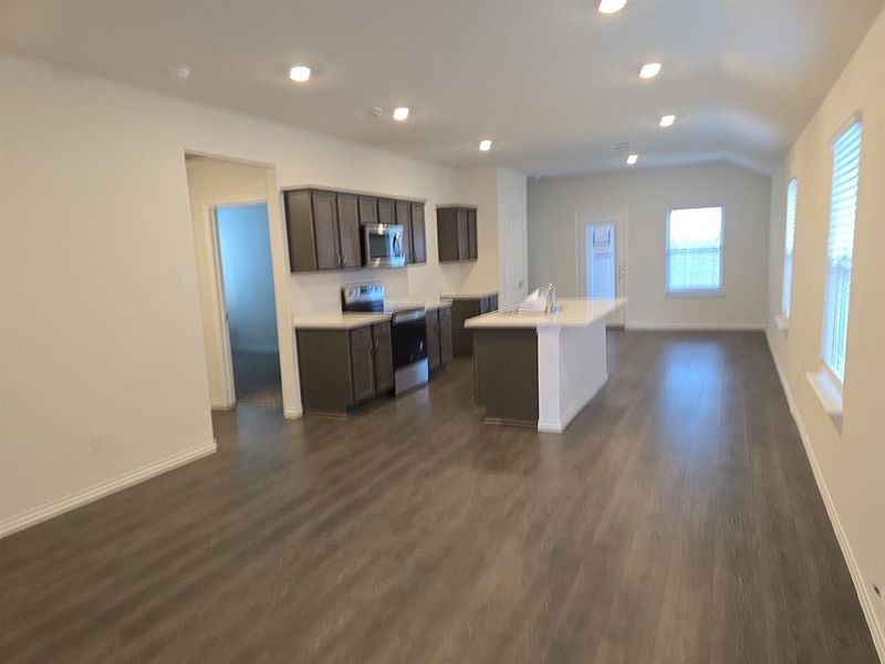 Kitchen featuring dark brown cabinets, electric range, dark wood-type flooring, a kitchen island with sink, and lofted ceiling