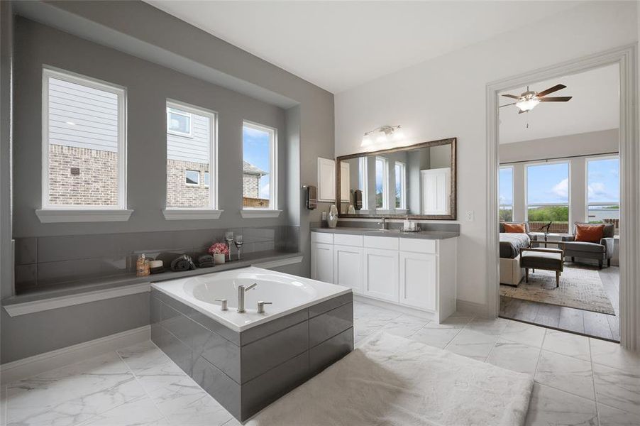 Bathroom with ceiling fan, a relaxing tiled tub, and vanity