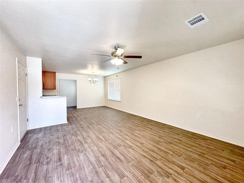 Unfurnished living room featuring hardwood / wood-style flooring, ceiling fan with notable chandelier, and a textured ceiling