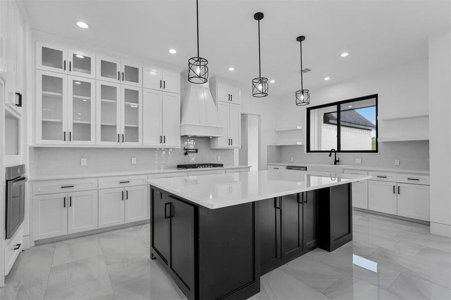 Kitchen featuring premium range hood, decorative light fixtures, oven, a center island, and white cabinetry