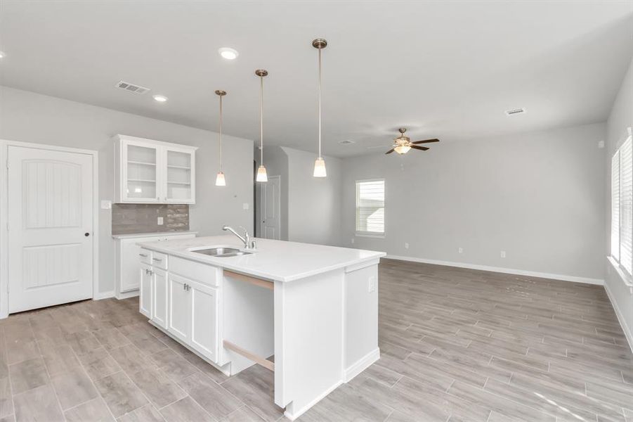 Step into this modern and spacious kitchen, a chef’s dream with its expansive island, pristine white cabinetry, and contemporary lighting fixtures. The open layout seamlessly connects the kitchen to the bright and airy living area, making it perfect for family gatherings and entertaining guests. **This image is from another Saratoga Home with similar floor plan and finishes, not the June floorplan.**