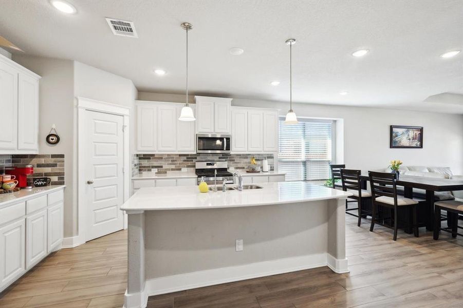 Kitchen with decorative light fixtures, light hardwood / wood-style floors, stainless steel appliances, and white cabinets