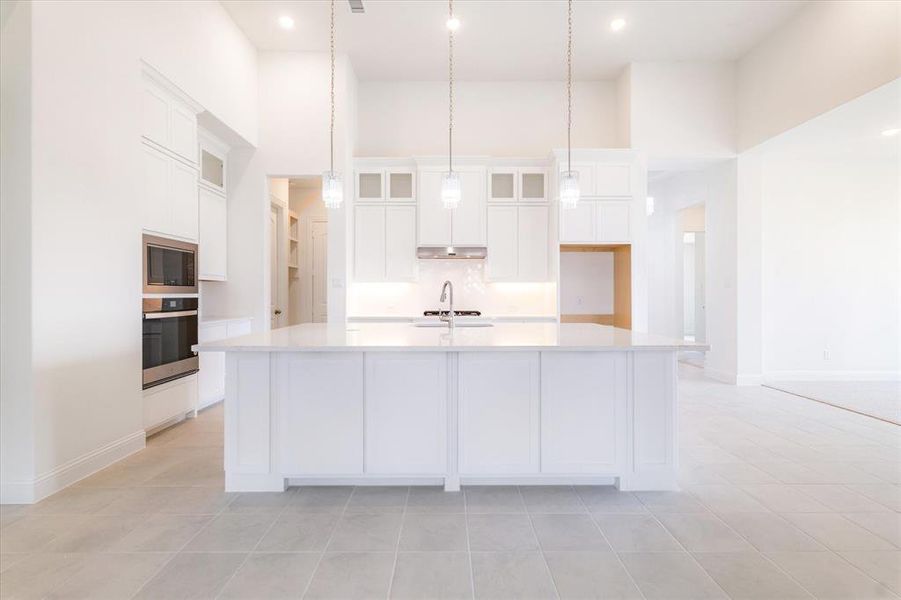 Kitchen featuring a towering ceiling, stainless steel appliances, tasteful backsplash, a kitchen island with sink, and light tile floors
