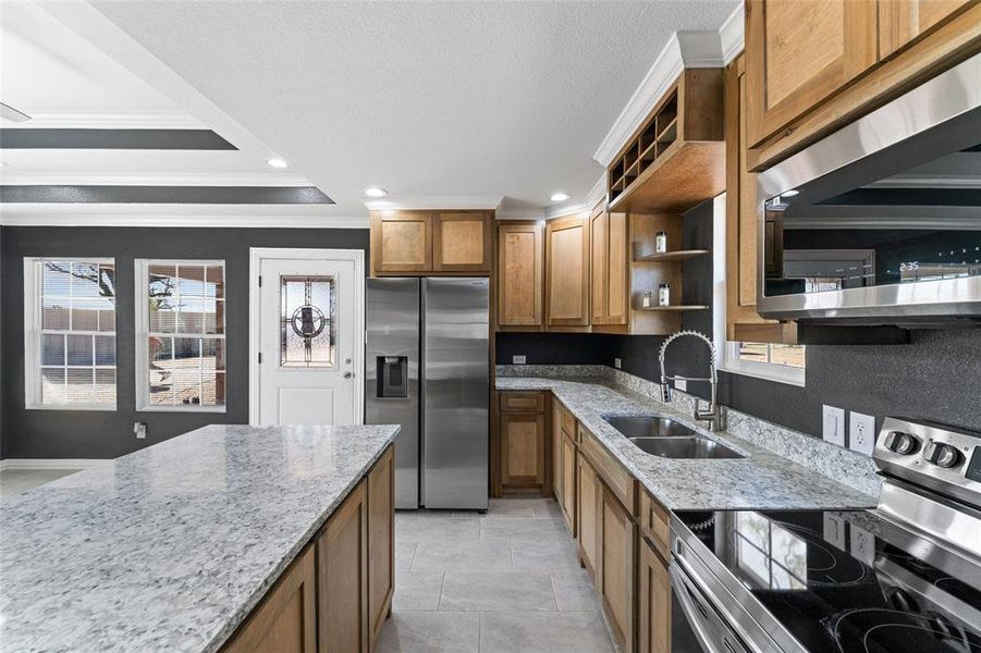 Kitchen with stainless steel appliances, ornamental molding, sink, light tile patterned floors, and light stone counters