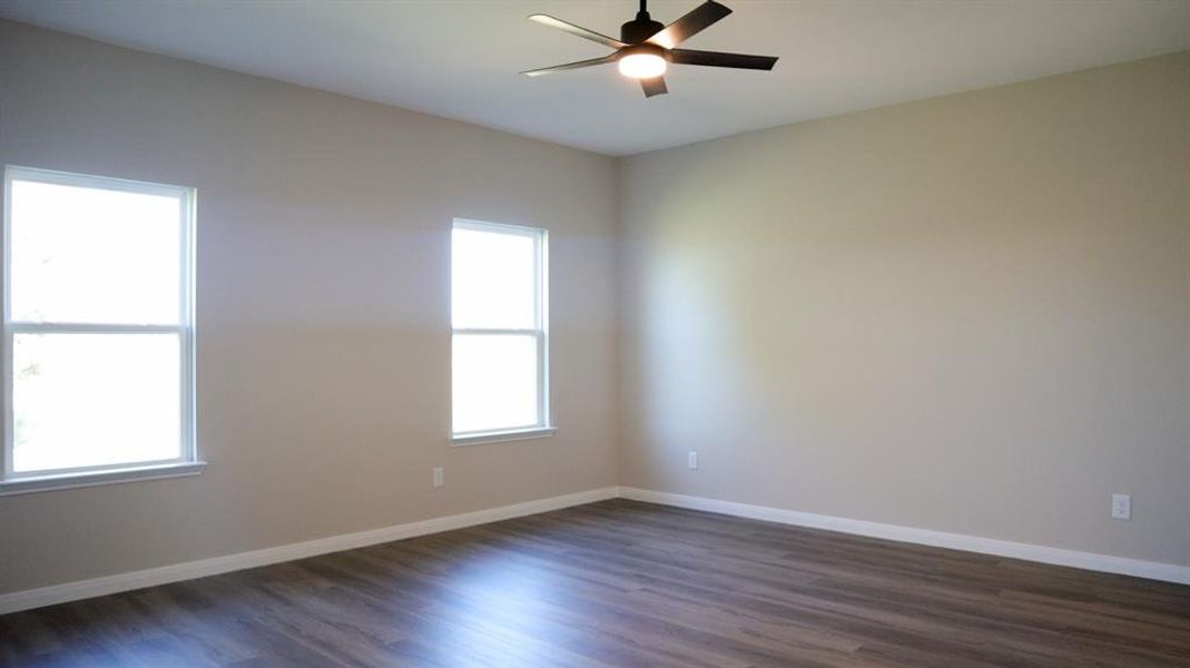 Empty room featuring dark hardwood / wood-style floors, ceiling fan, and a wealth of natural light