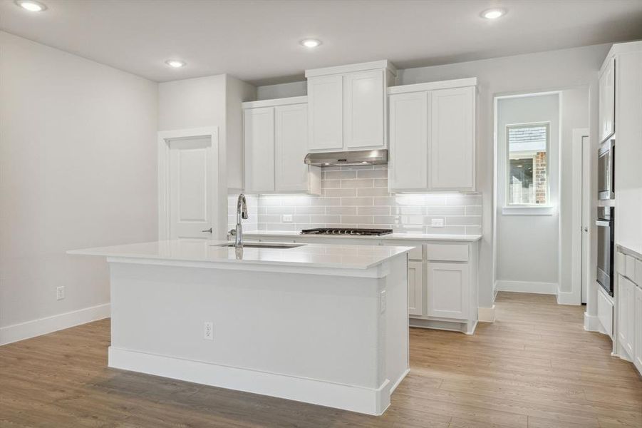 Kitchen featuring light hardwood / wood-style flooring, tasteful backsplash, sink, a kitchen island with sink, and white cabinetry