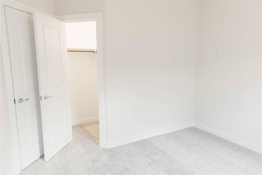 Unfurnished bedroom with a closet, light colored carpet, and a walk in closet
