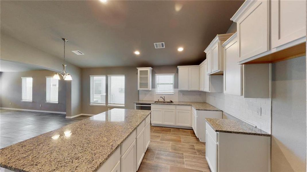 This view highlights the expansive kitchen and adjoining living area, featuring sleek granite countertops, abundant cabinetry, and a well-lit breakfast nook. The open-concept design promotes a sense of spaciousness and connectivity, perfect for both everyday living and hosting gatherings. This is a picture of an Elise Floor Plan with another Saratoga Homes.