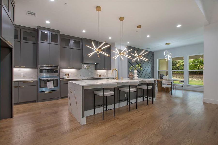 Kitchen with decorative light fixtures, light wood-type flooring, wall chimney exhaust hood, stainless steel double oven, and backsplash