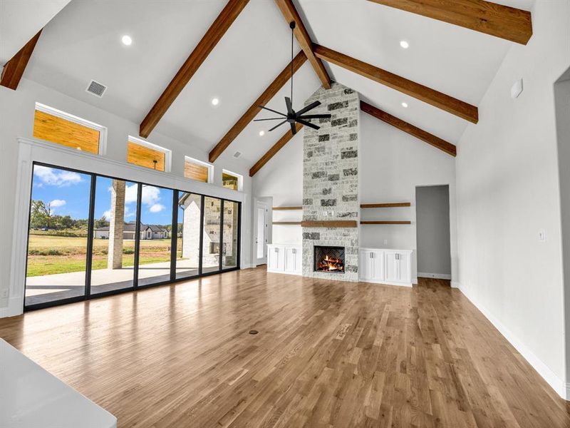 Unfurnished living room featuring beam ceiling, ceiling fan, high vaulted ceiling, light wood-type flooring, and a stone fireplace