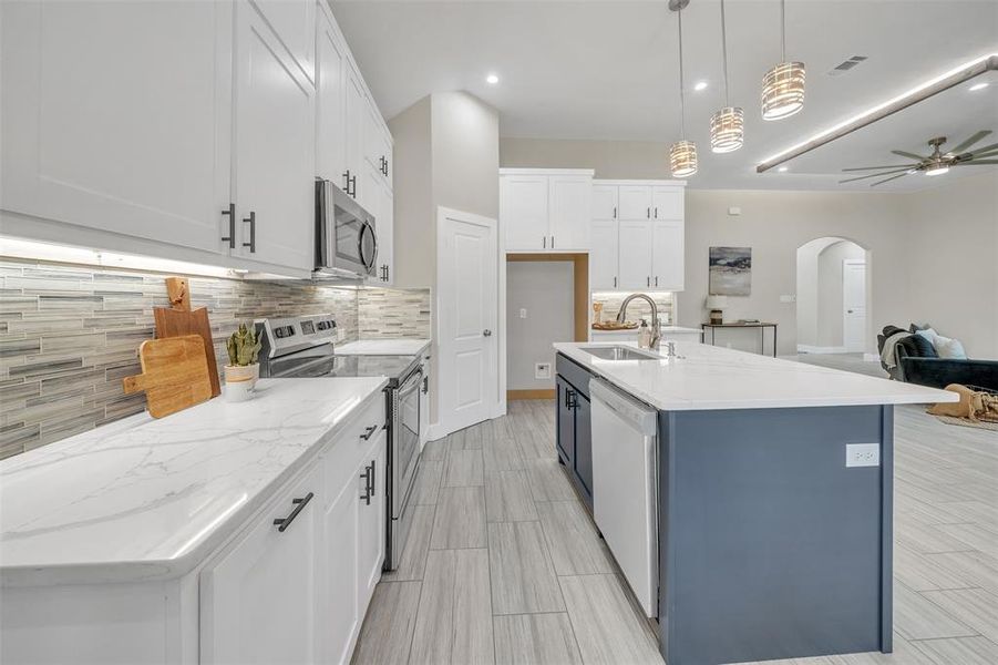 Kitchen with white cabinetry, ceiling fan, stainless steel appliances, decorative backsplash, and a center island with sink