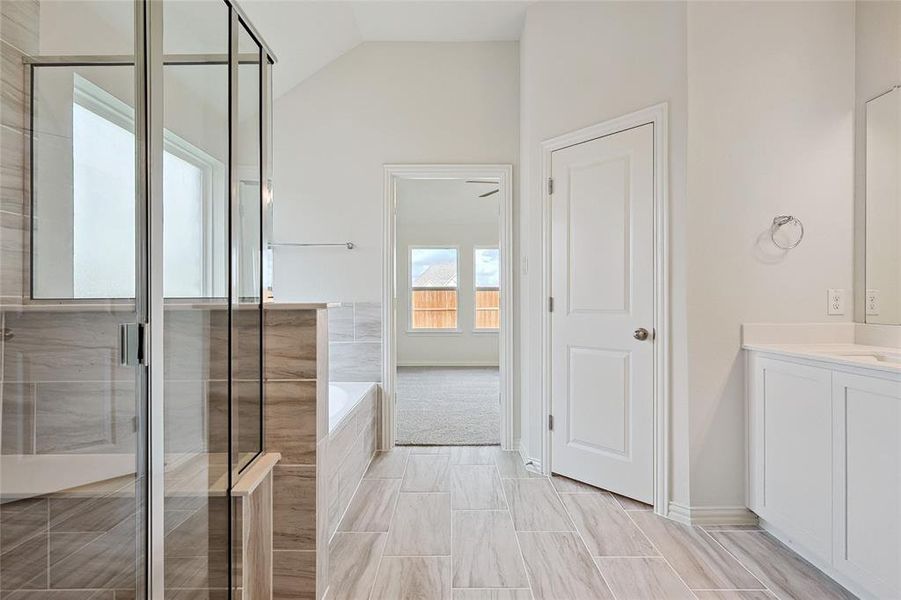 Bathroom with tile flooring, vaulted ceiling, independent shower and bath, and vanity