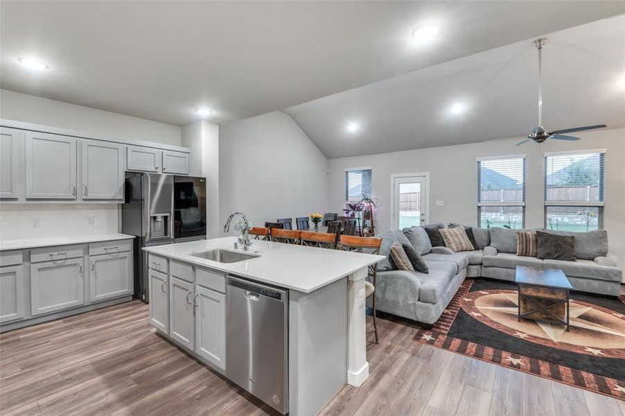 Kitchen with light hardwood / wood-style flooring, ceiling fan, stainless steel appliances, vaulted ceiling, and sink