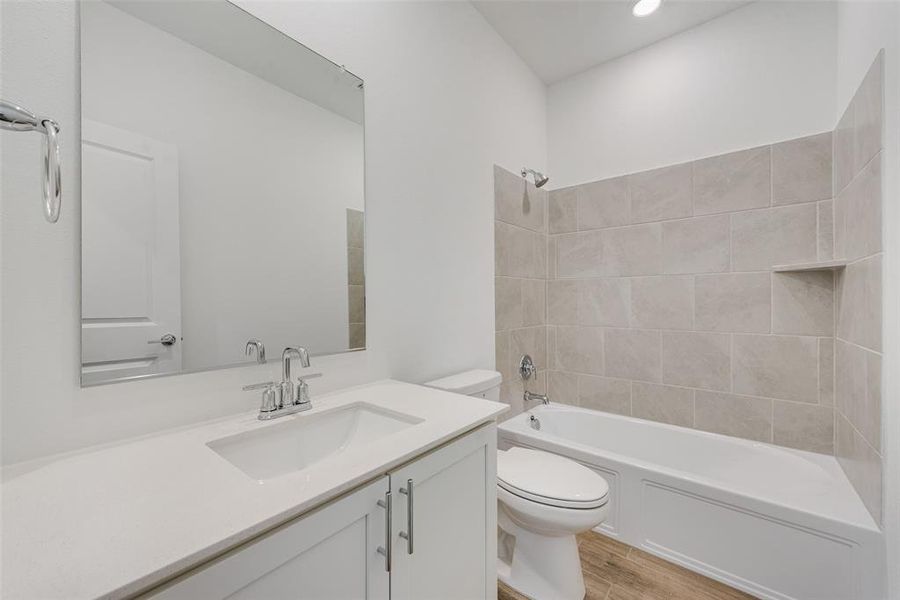 Full bathroom with tiled shower / bath, vanity, hardwood / wood-style flooring, and toilet