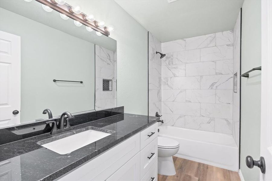 Full bathroom with vanity, toilet, tiled shower / bath combo, and wood-type flooring