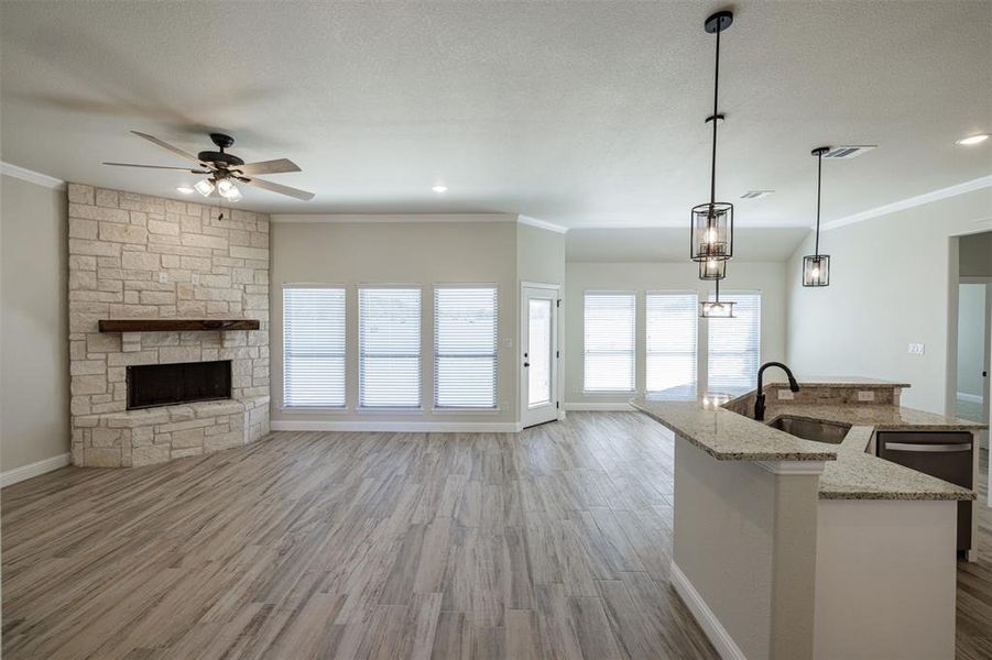 Kitchen featuring sink, a center island with sink, decorative light fixtures, light stone countertops, and light hardwood / wood-style floors