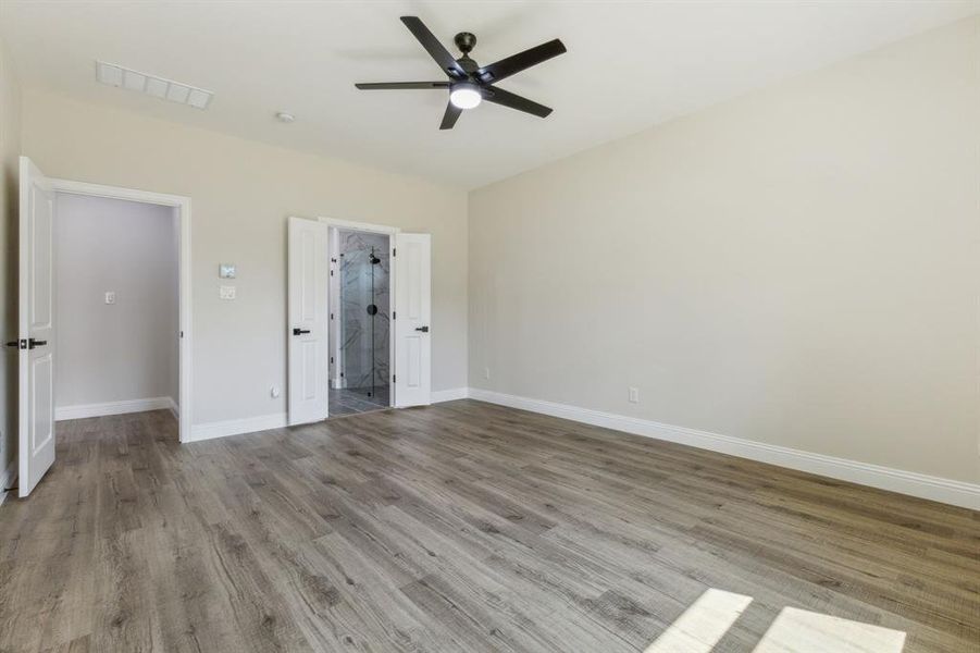 Unfurnished bedroom with ceiling fan, ensuite bathroom, and light hardwood / wood-style floors