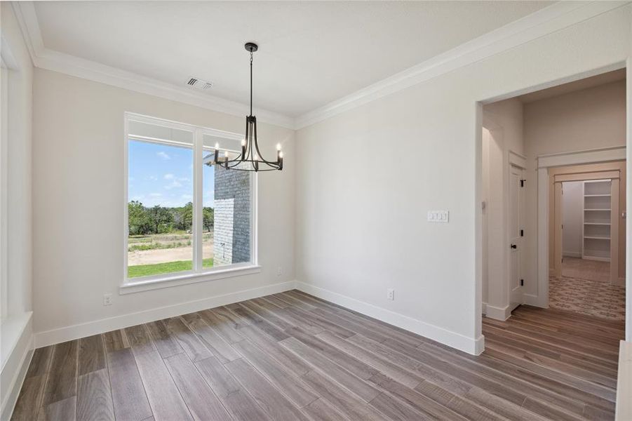 Unfurnished dining area featuring crown molding, hardwood / wood-style floors, and an inviting chandelier