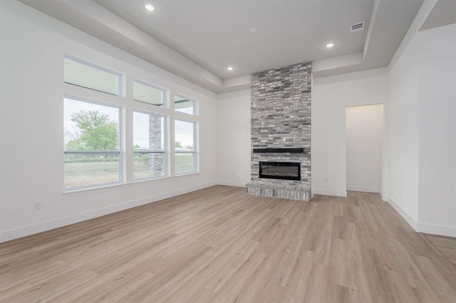 Unfurnished living room with a tray ceiling, light hardwood / wood-style floors, and a stone fireplace