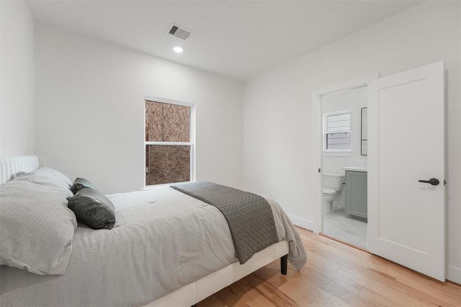 Bright and modern secondary bedroom features engineered hardwood floors, neutral custom color walls, and private secondary en-suite bathroom completed with window providing natural light.