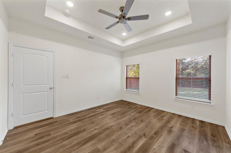 Empty room featuring hardwood / wood-style flooring, a tray ceiling, plenty of natural light, and ceiling fan