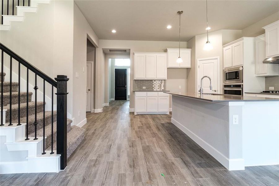 Kitchen with stainless steel appliances, decorative light fixtures, sink, hardwood / wood-style flooring, and white cabinets