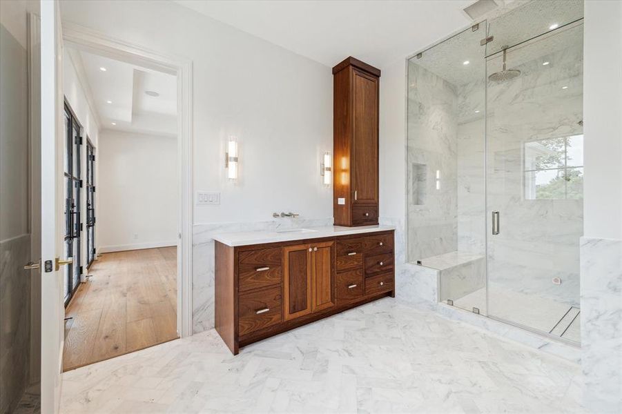 This second primary bathroom boasts handsome dark wood cabinetry that beautifully complements the stunning marble flooring, creating an elegant atmosphere. Illuminated by designer light fixtures, this space exudes sophistication while providing a luxurious retreat for relaxation and pampering.