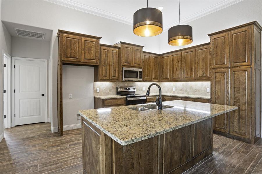 Kitchen featuring decorative light fixtures, sink, appliances with stainless steel finishes, backsplash, and a kitchen island with sink