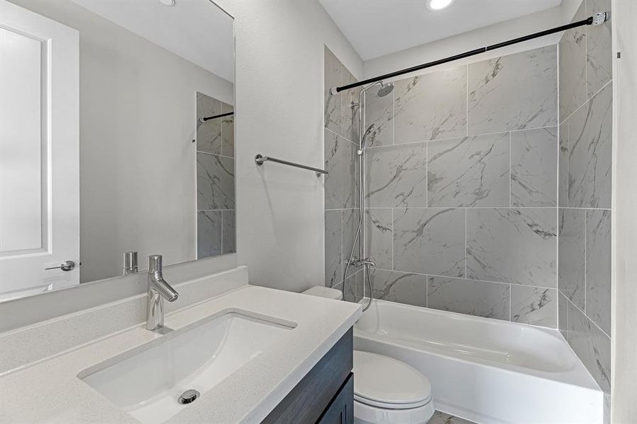 The secondary bathroom features chic tile flooring & a bath/shower combo with an exquisite tile surround, creating a stylish focal point. Warm wood cabinets offer both storage & inviting character, while the stunning quartz countertops elevate the space with a touch of sophistication.