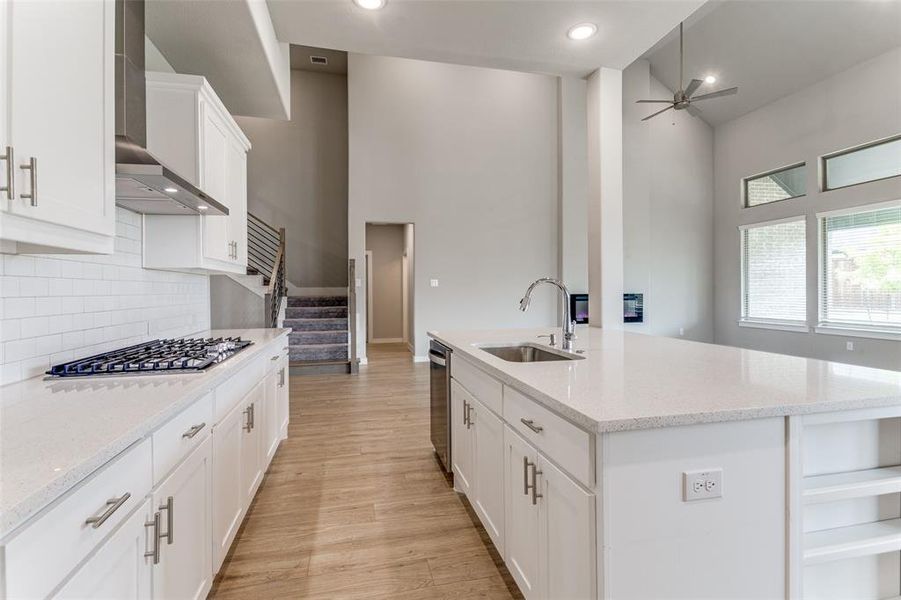 Kitchen with tasteful backsplash, light wood-type flooring, wall chimney range hood, stainless steel appliances, and sink